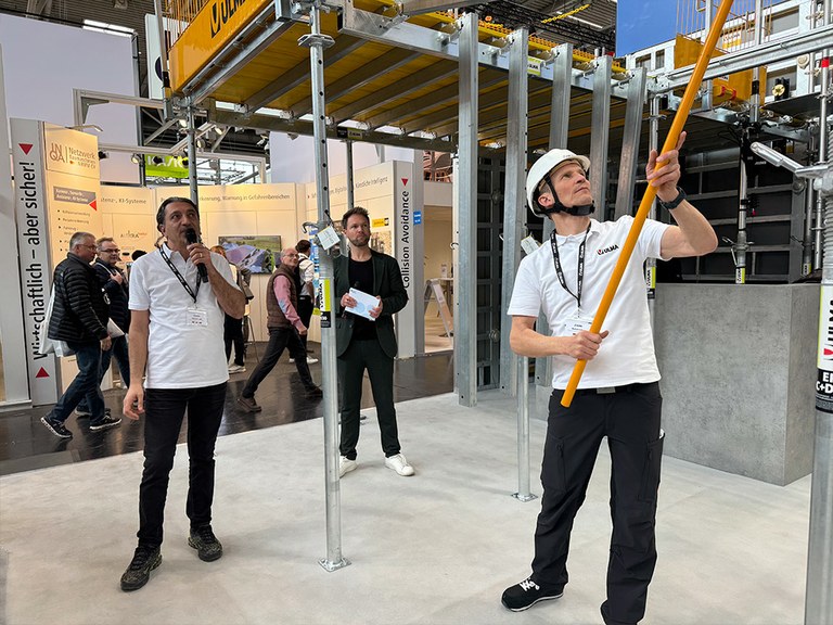 Am benachbarten Stand der BG Bau (B4, 103) konnten die Besucherinnen und Besucher die ULMA-Systeme „live on stage“ erleben. Im Rahmen der von Profi-Moderator Tobias Witton (m.) charmant präsentierten Shows demonstrierten Yildiray Eroglu (l.) und Michael Gräfe (r.) die sichere Performance der ONADEK TOP.